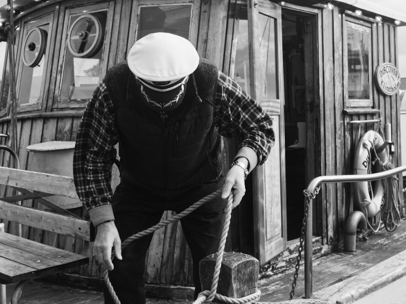 Captain in a peaked cap tying off a mooring line on a wooden boat